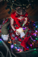 Blonde girl in a beautiful red dress unpacking Christmas gifts against the backdrop of a New Year tree