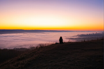 Fototapeta premium A person sits on a hilltop overlooking a sea of clouds during sunset, capturing a serene moment of reflection and solitude. Generative AI