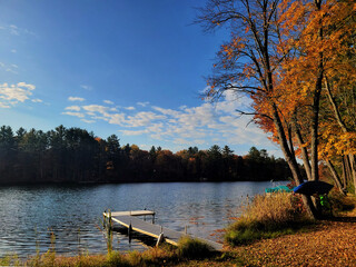Obraz premium Dock overlooking the lake on a sunny autumn day, bright fall colors in Michigan on the water, lakeside view with changing leaves 