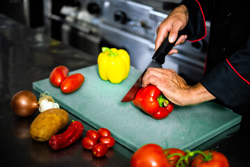 Chef in a professional kitchen meticulously chops vegetables on a cutting board, demonstrating...