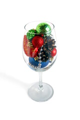 A glass goblet filled with Christmas balls stands on a white background.	
