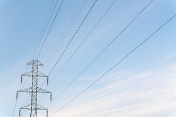 Wide-angle view of a high-voltage transmission tower rising against the backdrop of a blue sunset sky. The steel tower, framed by wires and cables, showcases the power of modern electricity.