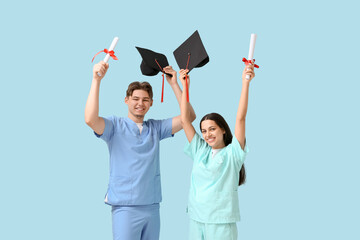 Happy medical graduate couple with diplomas and stethoscopes on blue background