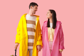Young couple in raincoats on pink background