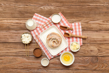 Plate with sweet cinnamon roll and different ingredients on wooden background