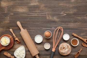 Sweet cinnamon roll and different ingredients on wooden background