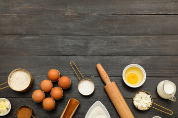 Different ingredients for preparing sweet cinnamon roll on black wooden background