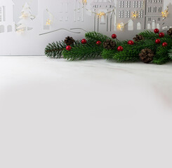 New Year's greeting card with fir branches and red berries on the background of a wooden city