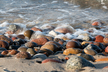 Close-up of sea water running onto picturesque multi-colored pebbles on the beach sand. Background....