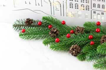 New Year's greeting card with fir branches and red berries on the background of a wooden city