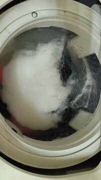 Dirty clothes spinning in a top-loading washing machine. Laundry and house keeping concept. Slow motion