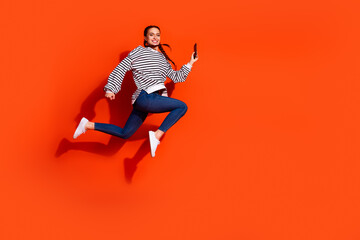 Young woman in striped pullover jumping joyously against vibrant orange background
