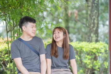 A Chinese Malaysian couple in their 30s sit and talk on a bench in a Chinese garden in Kuala Lumpur, Malaysia. A sunny afternoon in June 2024.