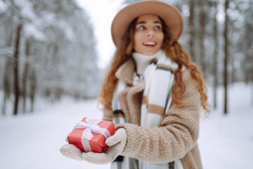 Portrait of happy woman holding festive red gift box in her hands background in winter forest. Winter holidays.