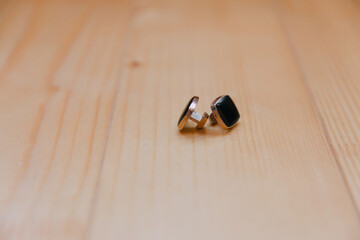 Two black earrings are sitting on a wooden table. The earrings are made of metal and have a black stone in the middle. The earrings are not attached to anything and are sitting on the table
