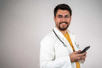 Natural black hair male doctor using smart phone standing isolated on grey wall background.