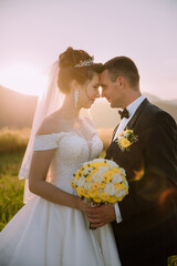 A bride and groom are standing together, with the bride holding a bouquet of yellow flowers. The...