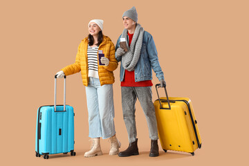 Cute young couple with suitcase and passports on beige background. Winter vacation concept