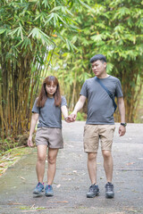 A Chinese-Malaysian couple in their 30s walk together in a green park with abundant water in Kuala Lumpur, Malaysia, on a sunny day in June 2024.