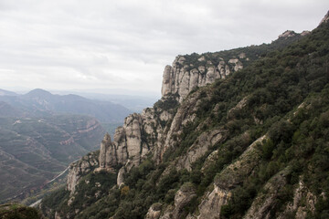 Huge rocky mountains covered with green forest. Clouds lie on the tops.