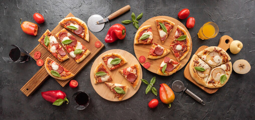 Pizza with pepperoni, basil and pears with glasses of wine on cutting boards on a dark background
