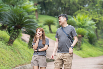 Fototapeta premium A Chinese-Malaysian couple in their 30s walk together in a green park with abundant water in Kuala Lumpur, Malaysia, on a sunny day in June 2024.