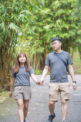 Obraz premium A Chinese-Malaysian couple in their 30s walk together in a green park with abundant water in Kuala Lumpur, Malaysia, on a sunny day in June 2024.