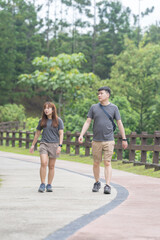 A Chinese-Malaysian couple in their 30s walk together in a green park with abundant water in Kuala Lumpur, Malaysia, on a sunny day in June 2024.