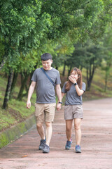 Fototapeta premium A Chinese-Malaysian couple in their 30s walk together in a green park with abundant water in Kuala Lumpur, Malaysia, on a sunny day in June 2024.