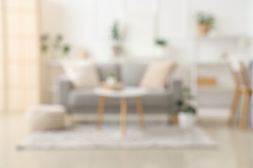 Blurred view of light living room with grey sofa, table and plants