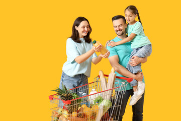 Happy family with full shopping cart and bottle of juice on yellow background © Pixel-Shot