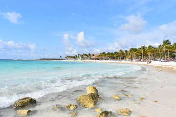  Picturesque tropical beach with white sand, rocky formations, and a row of swaying palm trees along the shore.