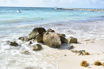 Idyllic tropical beach with white sand, rocky outcroppings, and a small boat on the horizon.