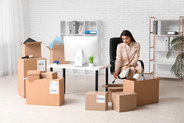 Fototapeta premium Young businesswoman packing things in office on moving day
