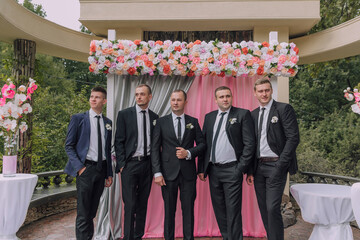 A group of men are standing in front of a pink curtain, dressed in black suits. Scene is formal and...