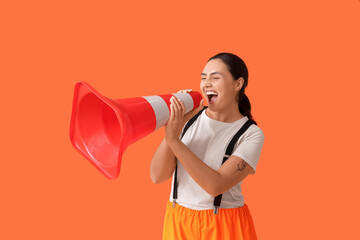 Young female construction worker yelling into traffic cone on orange background. Woman in male...