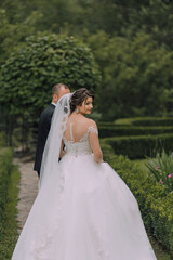 A bride and groom are walking down a path in a garden. The bride is wearing a white dress and a veil, while the groom is wearing a suit. The scene is peaceful and romantic