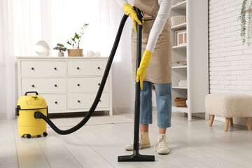 Young woman cleaning floor with vacuum cleaner at home