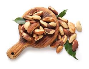 Wooden board with tasty Brazil nuts and leaves on white background