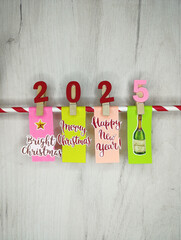 New year 2025 colored stickers on clothespins with congratulations on the new year and christmas on gray wooden background, red with white lollipop
