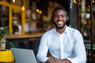 Obraz premium A cheerful man wearing headphones is working remotely on a laptop in a cozy cafe environment, embodying concepts of digital nomad lifestyle and connectivity.