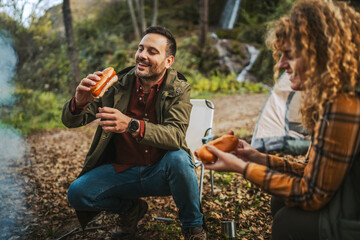 couple hiker backpacker prepare and eat hot dog in front tent