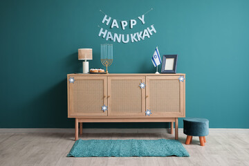 Wooden cabinet with menorah, donuts, flag of Israel and HAPPY HANUKKAH letter garland near blue wall