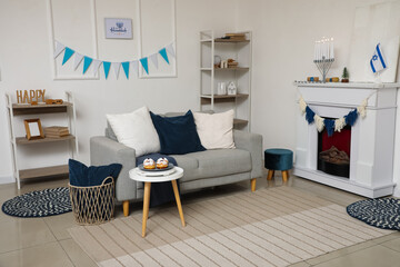 Interior of festive living room with grey sofa, donuts on coffee table and bunting. Hanukkah celebration