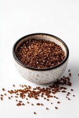 A bowl of brown granola sits on a white table, perfect for snacking or decorating