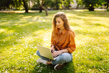 Young Woman sitting on grass ground, working on laptop. Online education, Freelance work, technology concept. Mobile Office.