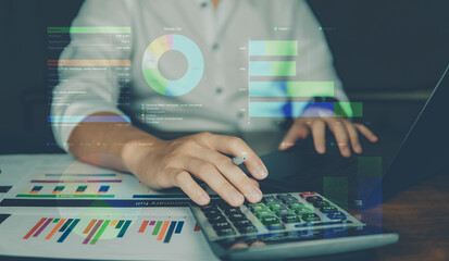 Business people use calculator with paper graph and laptop on working table, visual screen show business graph.