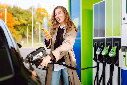 Young woman filling her car at the gas station. You can Online pay. Woman pays for a gas station using an app on her phone. 
