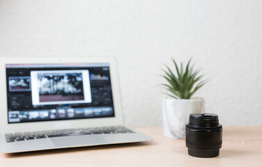 Photographer editing pictures on laptop with camera lens and plant on desk