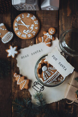 Delicious homemade gingerbread cookies in a glass jar with a note for Santa on the top. Tasty treat for Santa Claus. Wooden background, cozy festive home atmosphere, fir tree branches